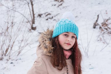 Kışın bej ceketli bir kız. Karlı bir kışta şapkalı ve kışlık kalın elbiseli bir kız poz veriyor..