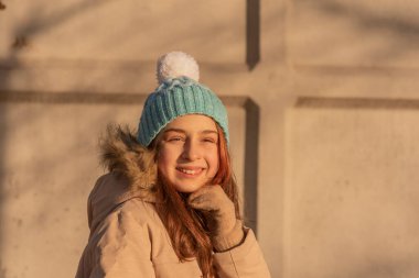 Kışın bej ceketli bir kız. Beyaz şapkalı ve kışlık sıcak elbiseli mavi elbiseli kız..