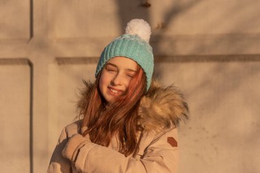 Kışın bej ceketli bir kız. Beyaz şapkalı ve kışlık sıcak elbiseli mavi elbiseli kız..