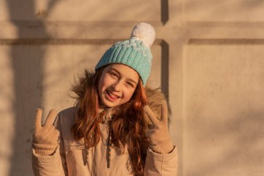 Kışın bej ceketli bir kız. Beyaz şapkalı ve kışlık sıcak elbiseli mavi elbiseli kız..