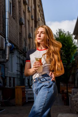 Kokteyl içme zamanı. Çok güzel bir kadın kokteyl içiyor. Tişört ve kot pantolonlu doğal sarışın.