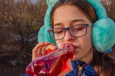 Kız sokaktaki bir şişeden içiyor. Kulaklık ve gözlüklü genç bir kız meyve suyu içiyor.