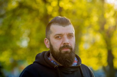 Bulanık arka planda sakallı, güneşli, kapüşonlu adam. Siyah kapüşonlu sakallı adam.