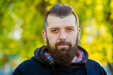 Bulanık arka planda sakallı, güneşli, kapüşonlu adam. Siyah kapüşonlu sakallı adam.