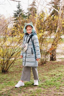 Açık havada, tüylü kulaklıkları ve doğa arka planında şık bir ceketi olan genç bir kız. Bakıyor