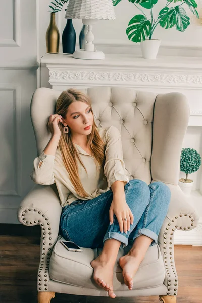 Sarışın oturma odasında bir sandalyeye ya da kanepeye oturdu. Profesyonel makyajlı kız..