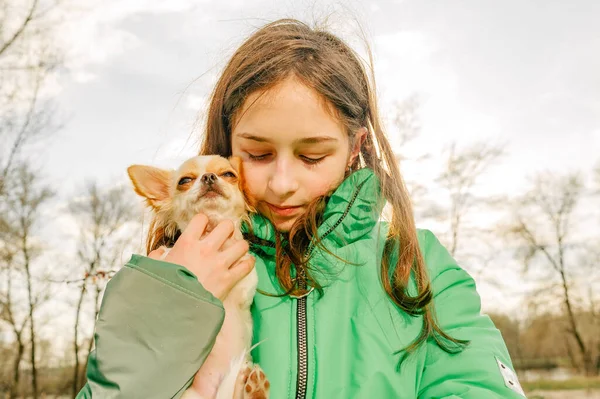 Teenager girl with chihuahua. girl in green jacket with puppy in her arms. Chihuahua dog with girl.