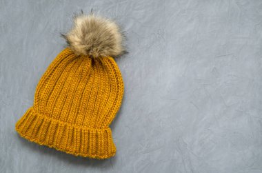 Küçük şirin örülmüş, hardal renginde kürk ponponlu sıcak şapka gri beton arka planda metin için yer var.