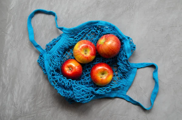 blue mesh eco zero waste shopping bag with fruit red apples, top view on ultimate gray background, close up with space for text