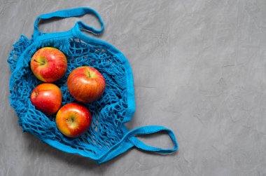 Mavi ağlı sıfır atık poşeti, meyveli kırmızı elmalar, üst görünüm nihai gri arkaplan, metin için boşluk ile kapatın