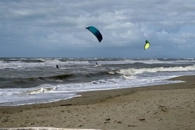 İtalya sahilinde uçurtma. Torre del Lago sahilindeki uçurtmacılar, Toskana, İtalya. Bazıları sudan çıkmakta zorlanıyor. Akdeniz.