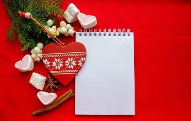 Kutlama kompozisyonu Notepad, beyaz süslemeli kırmızı ahşap kalp ve kırmızı arka planda yeşil köknar dalları. Noel ve Sevgililer Günü konsepti.