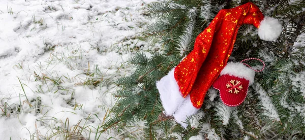 サンタクロースの帽子と小さな赤いミトンは雪で覆われたモミの木に横たわっています テキストのスペース — ストック写真