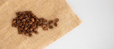 Kahve çekirdekleri ve çuval bezi gri bir arka planda yatıyor..