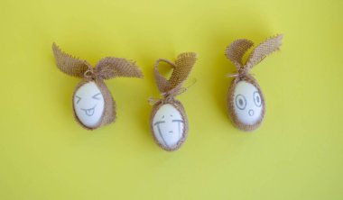 Sarı arka planda çuval bezli komik yüzlü beyaz yumurtalar. Paskalya Konsepti.