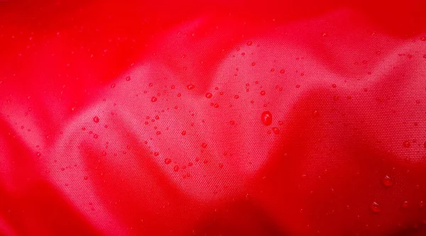 Large drops of water on a red textile with a waterproof effect. Water-repellent impregnation. Texture drops on the fabric.