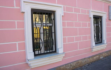 Beyaz pencereli ve parmaklıklı pembe cephenin yan görünümü.