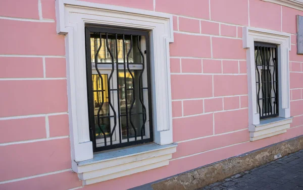 Beyaz pencereli ve parmaklıklı pembe cephenin yan görünümü.