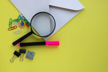 Sarı arka planda, kırtasiye malzemeleri, bir büyüteç, bir zarf. Okul, ofis, seyahat kavramı..