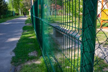 Metal fence painted in green color.Metal wire grating along the playground in the park.