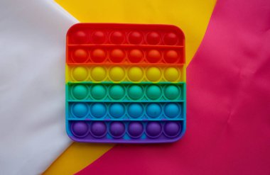 Gökkuşağı oyuncağı pembe ve sarı beyaz kumaşın arka planında yatar. Mavi ve Turuncu komik etkileşimli stres önleyici silikon oyuncaklar. Patlat..