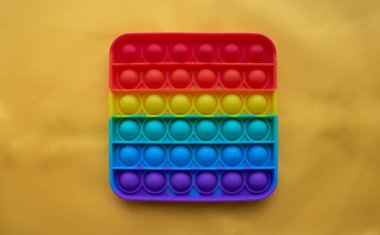 Bir gökkuşağı oyuncağı sarı kumaşın arka planında yatar. Mavi ve Turuncu komik etkileşimli stres önleyici silikon oyuncaklar. Patlat..