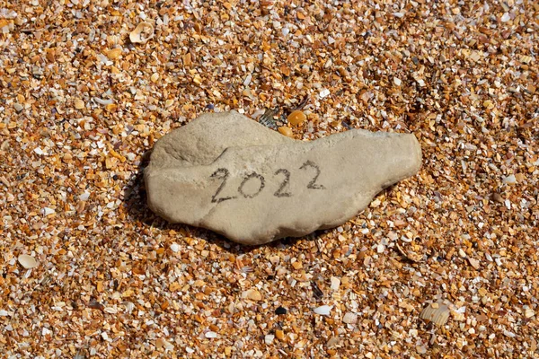 The numbers 2022 on a small gray stone on the background of a small shell. The concept of the New Year 2022. Summer holidays and sea trips.