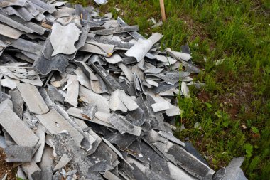 Gri yazı tahtası, farklı şekil ve boyutlarda parçalara ayrılmış, çimlerin üzerinde yakın plan bir kazıkta yatıyor. İnşaat atıkları. Çevre kavramı.