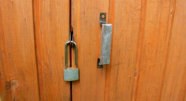 Küçük asma kilidi olan kahverengi, açık ahşap bir kapı..