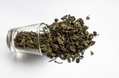 Kurumuş çay yaprakları küçük bir bardaktan beyaz arka plana saçılmış..