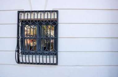 Evin beyaz duvarında siyah metal parmaklıklar olan küçük, kapalı bir pencere..