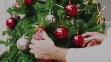 Kırmızı top tutan Asyalı adam Noel ağacını süslüyor ve yeni yılı evdeki oturma odasında kutluyor. Noel kutlaması kavramı.