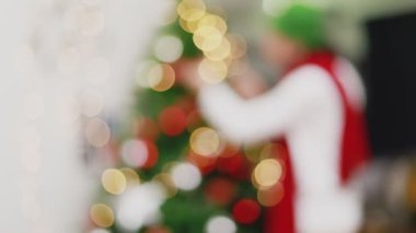 Arka planda bulanık Asyalı bir adam elinde küçük bir hediye kutusu tutarak Noel ağacını süslüyor ve yeni yılı evdeki oturma odasında kutluyor. Noel kutlaması kavramı.