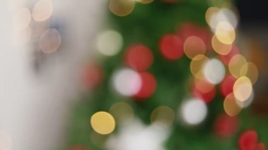 Arka plan ışıklarını bulanıklaştıran kamera Noel ağacını süslüyor ve yeni yılı evdeki oturma odasında kutluyor. Noel kutlaması kavramı.
