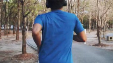 İzleme fotoğrafı: Parkta koşarken kulaklık takan Asyalı atlet müzik dinliyor. Sağlıklı yaşam tarzı kavramı.