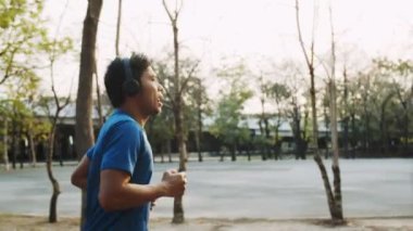 Asyalı bir adam parkta koşuyor ve güzel bir günbatımında müzik dinliyor..