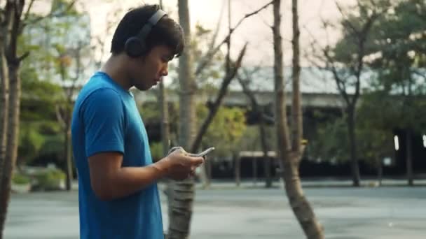 亚洲男人在公园里散步时 用智能手机在室外训练后休息 — 图库视频影像