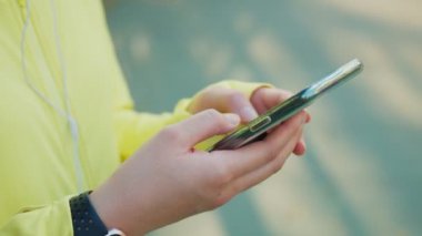 Sporcuyu kapatırken akıllı telefon kullanarak sosyal medya kaynaklarını kontrol et. Şehir sokaklarında koştuktan sonra dinlenme zamanı..