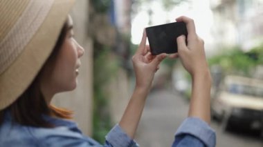 Eski bir şapka takan Asyalı kadın akıllı telefon kullanarak Bangkok Tayland 'da küçük bir sokakta fotoğraf çekiyor ve yaz tatili tatili için Güney Doğu Asya' nın tadını çıkarıyor..