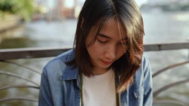 Tatilde Tayland 'da Chao Phraya Nehri' nin yanında otururken akıllı telefon cihazları kullanarak sosyal medya paylaşımı yapan Asyalı kadını kapatın..