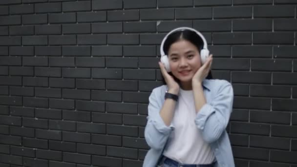 在泰国曼谷的一条小街上 亚洲少女带着耳机 听着音乐和跳舞 度过了一个愉快的暑假 — 图库视频影像