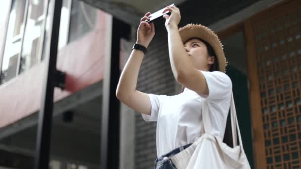 在旧城的一条小街上 漂亮的亚洲女人头戴软礼帽 用智能手机拍照 青少年假期旅途愉快 — 图库视频影像