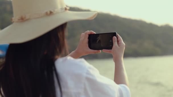 幸せなアジアの10代の女性は ビーチの美しい夕日に写真を撮るスマートフォンを保持 ライフスタイル旅行休暇夏のコンセプト — ストック動画
