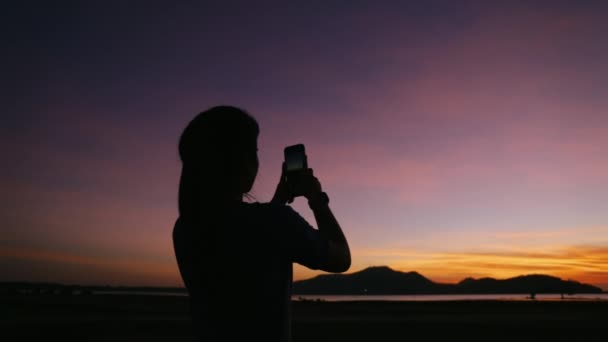 アウトドアフィットネスと健康的なライフスタイルのコンセプトを実行した後 バニラの空に美しい夕日を撮影スマートフォンを使用して若いアジアの女性選手 — ストック動画