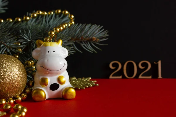 Figurka krowy otoczonej świątecznymi dekoracjami i choinką na czerwonym i czarnym tle, kartka świąteczna 2021 rok byka — Zdjęcie stockowe