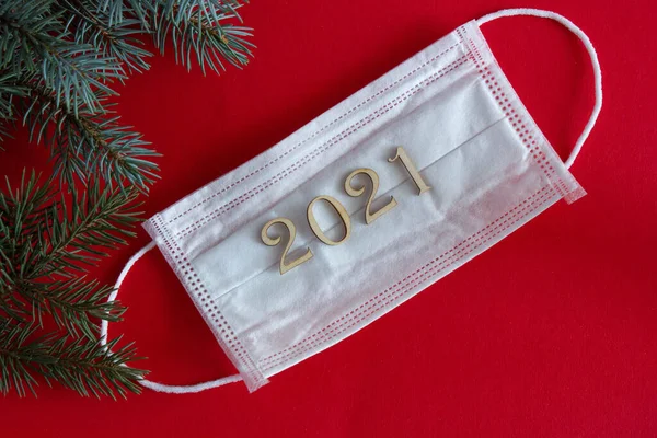 2021 numaralı tıbbi maske. Kırmızı arka plan, köknar dalları, yeni yıl pandemik tatil fikri.
