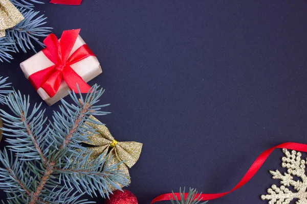 Fondo elegante de Navidad con un lugar para una inscripción, juguetes de Navidad y ramas de un árbol de Navidad sobre un fondo oscuro en los bordes, un regalo con una cinta roja — Foto de Stock