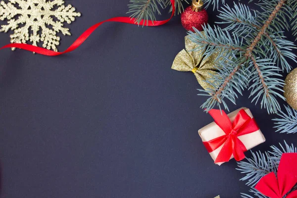 Noel arkaplanı, yazıtlar, Noel oyuncakları ve arka planda bir Noel ağacının dalları olan kırmızı kurdeleli bir hediye.