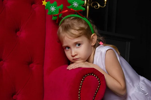 Kırmızı bir sandalyenin koluna yaslanmış, Noel ağaçlarıyla bir çemberde dalgın bir kız Noel 'i bekliyor.