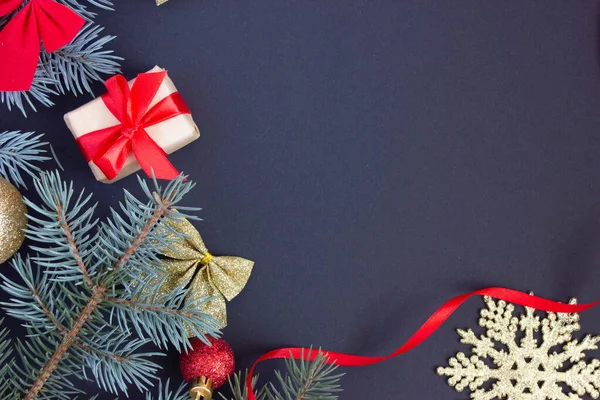 Fondo elegante de Navidad con un lugar para una inscripción, juguetes de Navidad y ramas de un árbol de Navidad sobre un fondo oscuro en los bordes, un regalo con una cinta roja — Foto de Stock